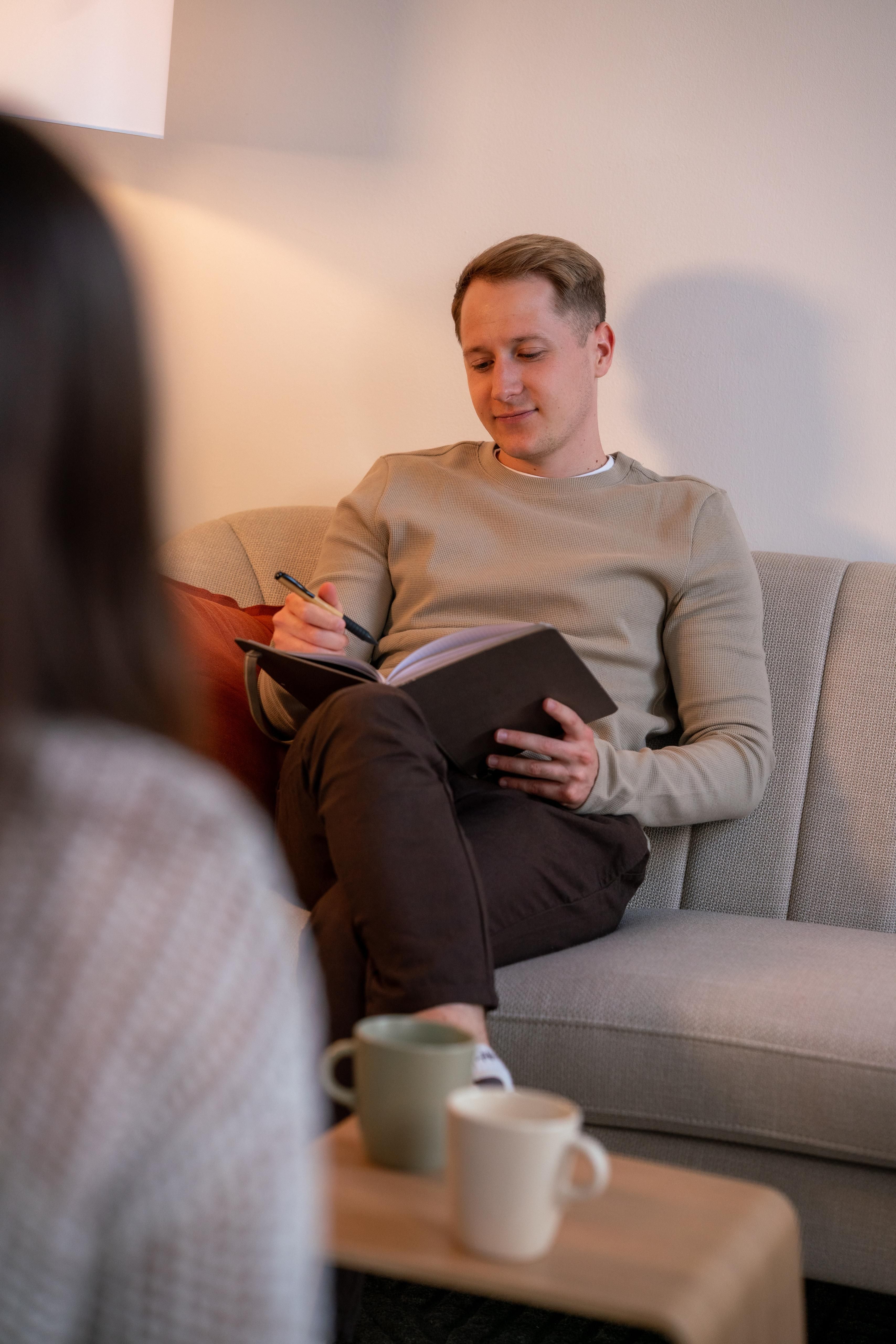 Felix Steurer im therapeutischen Gespräch, Notizen machend, einer Klientin gegenüber